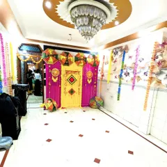 A wide view of the Haldi decoration setup in a home, showing the main backdrop and colorful flower strings hanging from the ceiling.