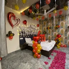 For this anniversary surprise, I created a full room transformation. The setup includes a custom foil balloon message with the couple's names, a romantic rose petal pathway leading to the bed, and a mix of red, yellow, and black balloons for a vibrant, celebratory feel.