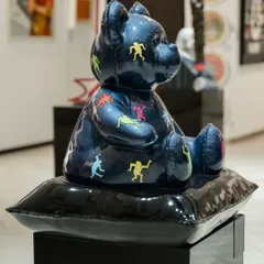 A side view of 'Ted – Ode To Keith Haring' by Mr Apex. This FRP resin sculpture, finished with chrome plating and candy paint, turns the teddy bear into a symbol of innocence with an edge, seated on a glossy black cushion.