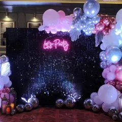 A fun and energetic party corner with a black sequin backdrop and a 'Let's Party' neon sign. The setup is completed with a garland of metallic balloons and silver disco balls on the floor, setting the mood for a night of dancing.