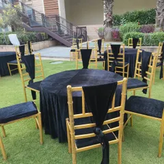 An elegant black and gold theme for event seating. The round tables are covered with black velvet, and the gold chairs are accented with black drapes for a very formal and chic look.