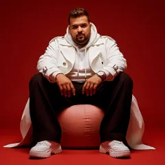 A modern, streetwear look against a bold red background. My style is always evolving, just like my music, which spans genres from Soul Techno to UK Punjabi.