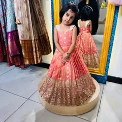 A frontal view of this gorgeous custom frock. The peach brocade fabric has a beautiful sheen, complemented by the wide, intricately woven gold border that gives it a luxurious, festive look.