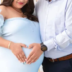 A simple, beautiful gesture. The couple forms a heart with their hands on the baby bump, a universal symbol of their love for the little one on the way.