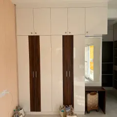 A floor-to-ceiling wardrobe with a dual-tone finish of white laminate and wood grain. The design includes an integrated dressing table, making it a complete and space-efficient solution.
