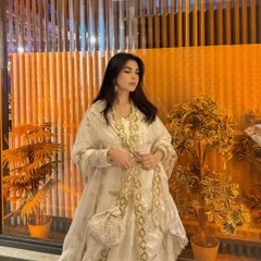 Modeling a beautiful white and gold embroidered Anarkali suit. The warm, golden background lighting makes the outfit's details pop, creating a rich and festive mood.