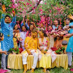 A wide shot of the couple being showered with pink flower petals by their loved ones during a joyous and colorful Haldi celebration.