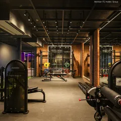 The strength training area is equipped with a variety of machines and free weights to suit a full-body workout. The exposed brick and modern lighting create a motivating, urban gym atmosphere.