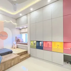 A full view of the kids' room, showing the platform bed with integrated storage and a whimsical, backlit cloud-shaped false ceiling detail. The wardrobe features pops of color in its open niches.