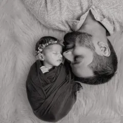 A father and child, captured in a classic black and white composition. This artistic style emphasizes the bond and the contrast between the strong father and his delicate baby.