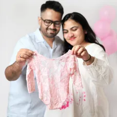 The happy couple holds up a delicate pink onesie, announcing they are expecting a daughter. Their joyful expressions say it all.