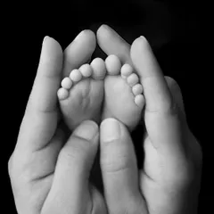 A black and white close-up of a parent's hands cupping their baby's feet. The dramatic lighting highlights every tiny wrinkle and detail.