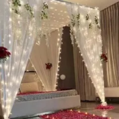 For a clean and elegant look, I can create a beautiful bed canopy using white drapes and fairy lights. A path of rose petals on the floor adds that final romantic touch for a first night or anniversary decoration.