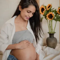 A quiet moment for the mother-to-be, looking down at her baby bump. The sunflowers in the background add a cheerful pop of color to this indoor studio-style shot.