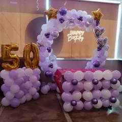 Celebrating a 50th birthday in style with a purple and white color scheme. This setup includes a circular balloon arch, a table decorated with balloons, a "Happy Birthday" neon sign, and giant gold foil balloons for the number '50'.