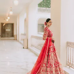 A portrait of the bride in a classic red lehenga, looking out a window. The soft, natural light and elegant pose create a feeling of timeless grace.