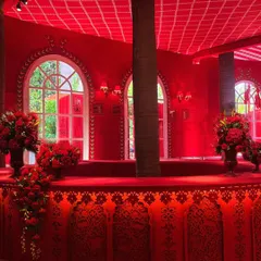 A custom-built bar for the 'Laal Ishq' event. The structure incorporates the theme's signature red color and intricate patterns, with large arched windows behind it offering a view of the gardens.