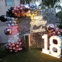 An outdoor 18th birthday celebration featuring a personalized neon sign, a silver sequin wall, and a stylish balloon arch in metallic and pastel colors.