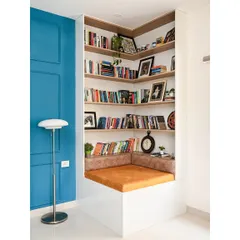 A different angle of the reading nook, showing how it is neatly tucked into a corner of the room. The combination of the bright orange cushion and the deep blue wall creates a vibrant and inviting space.