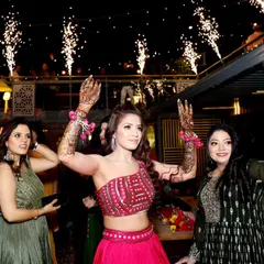 The bride enjoying her Sangeet night with friends, dancing with her hands in the air. The sparklers in the background add to the festive, celebratory mood.
