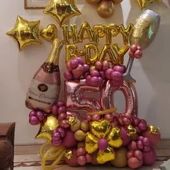 A festive balloon bouquet celebrating a 50th birthday. This arrangement uses pink and gold chrome balloons, large '50' foil numbers, and champagne bottle and glass foil balloons for a celebratory touch.