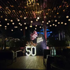 Celebrating a 50th birthday calls for something truly special. For this milestone party, I designed a sophisticated outdoor lounge setting with a dramatic sequin backdrop, a custom neon sign, and large marquee numbers, all under a canopy of warm string lights.