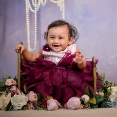 A beautiful floral swing setup. The baby is nestled in a seat surrounded by a cascade of pink and white flowers, with elegant pearls hanging from above, creating a soft and classic portrait.