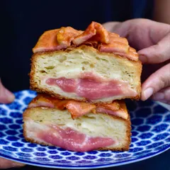 A cross-section of our Guava Kouign Amann, a laminated and caramelised croissant pastry. It's filled with a sweet custard and pink guava jam, then topped with fresh guava and a hint of chilli caramel.