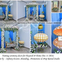 A traditional naming ceremony decor for Heyansh at home. The setup features a beautiful floral swing for the baby and a unique seashell prop for the name reveal.