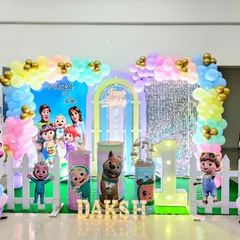 A cheerful and colorful Cocomelon theme, a favorite for toddlers' birthdays. This setup includes character cutouts of JJ and friends, a rainbow pastel balloon arch, a large light-up number '1', and a white picket fence for a playful look.