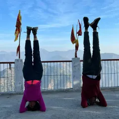 Two practitioners finding balance and strength together in a supported headstand during our Rishikesh retreat.