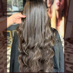 Shades that whisper luxury, tones that scream confidence. This long, wavy style showcases a cool-toned balayage with expertly placed highlights.