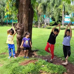 Children practicing Vrikshasana (Tree Pose) next to a real tree. My kids' yoga classes are all about making yoga fun and relatable, connecting the practice to the world around them.