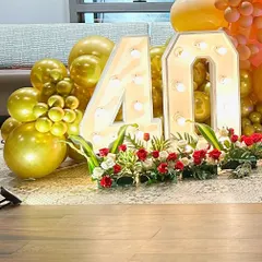 A close-up of a 40th birthday celebration, showing the large marquee '40' decorated with flowers and surrounded by gold balloons.