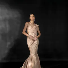 A full-length studio shot for Nikhil Thampi's 'GLEAM' collection, featuring a model in a shimmering mermaid-style gown against a dark, moody backdrop.