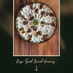 Our Dozen Spiced Curried Hummus, a unique fusion dip that brings together Middle Eastern and Indian flavors, garnished with caramelized onions and edible flowers.