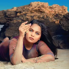 Lost in the rhythm of the waves. A beautiful beach portrait with the model lying on the sand, her striking blue eyes looking directly at the camera.