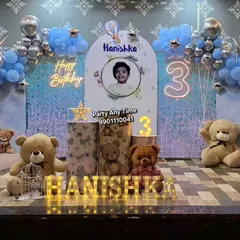 I create magical teddy bear themed parties perfect for a young child's birthday. This setup features a shimmer wall, a moon prop with a teddy, multiple teddy bears, custom cake stands, and a blue and silver balloon arch, complete with a neon birthday sign.