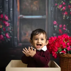 Such a happy little guy! This toddler's joyful expression is perfectly captured as he claps his hands, sitting in a box against a beautiful floral backdrop.
