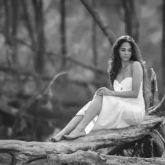 A black and white version of an editorial bridal portrait. The monochrome tones emphasize the texture of the forest and the model's contemplative expression, creating a powerful, timeless image.