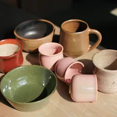 An assortment of cups, bowls, and mugs in earthy green and soft pink glazes, created by students in our 7 week wheel throwing course.