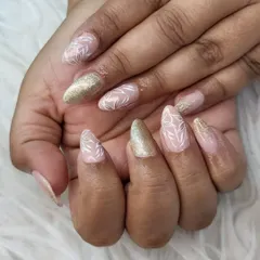 This elegant almond-shaped set combines a soft nude base with hand-painted white leaf patterns and accent nails in a brilliant gold glitter. It’s a popular choice for brides and bridesmaids alike.