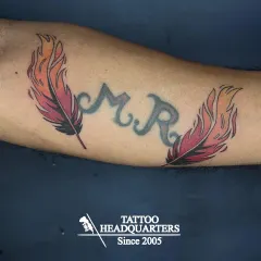 A great example of a creative cover-up. We used two vibrant, fire-themed feathers to beautifully transform the original "M.R." initial tattoo.