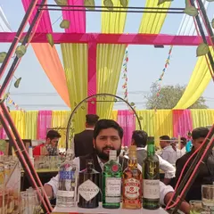 Our bartender ready to serve at a daytime Holi celebration, with a colorful canopy and a full selection of premium spirits.
