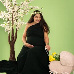 A peaceful moment captured in a classic seated pose. The one-shoulder black gown provides a simple elegance, complemented by the soft floral elements in the scene.