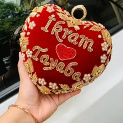 My heart-shaped bridal clutch, made from rich red velvet, is one of my favorite babies. I hand-embroider your names, like 'Ikram' and 'Tayaba' here, to make it a keepsake you'll treasure long after the wedding day. It's perfect for holding your phone and lipstick.