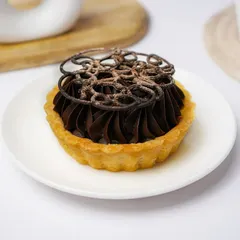 An artisanal chocolate tart with intricate piping and a dusting of cocoa, presented elegantly on a white plate.