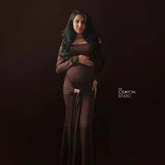 A full length portrait in a form fitting brown gown. Her direct gaze and confident stance project strength and beauty in this minimalist studio setting.