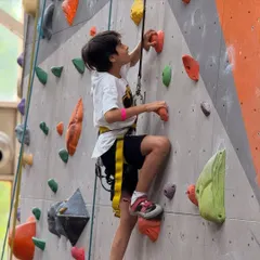 A young boy carefully plans his next move on a beginner friendly route. Climbing is a great way for kids to develop problem solving skills and physical coordination.