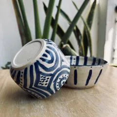 A pair of hand-painted bowls, perfect for snacks or soup. The bold, graphic patterns in blue and white were painted by a student, showing how you can personalize your own tableware.